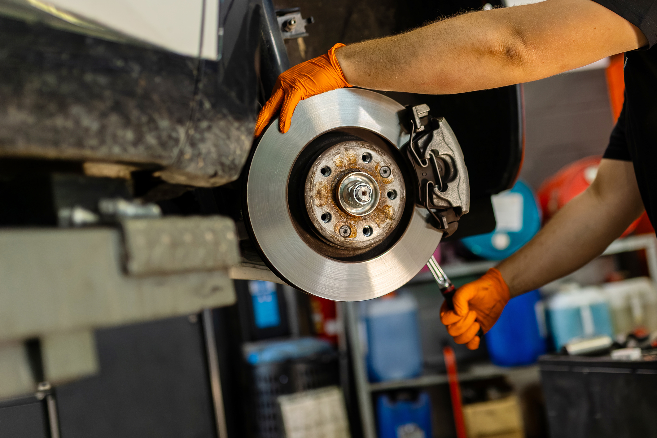 Mechanic in orange gloves installs or repairs a car brake disc.